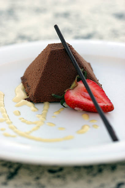 Chocolate Pyramid Chocolate pyramid cake dusted with cocoa powder, presented on a white plate with a sliced strawberry and dark chocolate straw wedding cake close up macro stock pictures, royalty-free photos & images