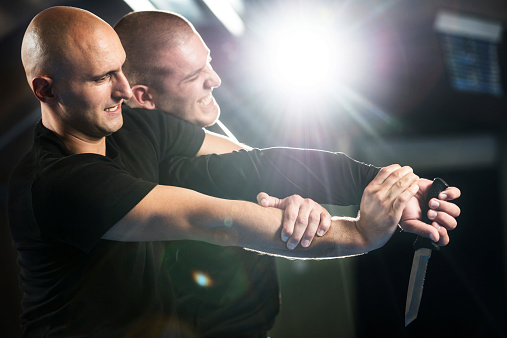 Mid adult martial artist self-defending from an attacker who is holding a knife.  