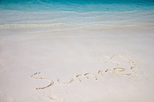 Handwriting of summer word on the beach backgrounded with clear blue sea