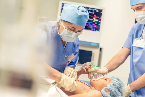 Young girl with oxygen mask lying on bed in operating room with doctors and nurses.