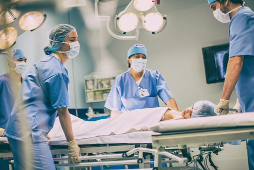 Young girl lying on bed in operating room surrounded with nurses or doctors.