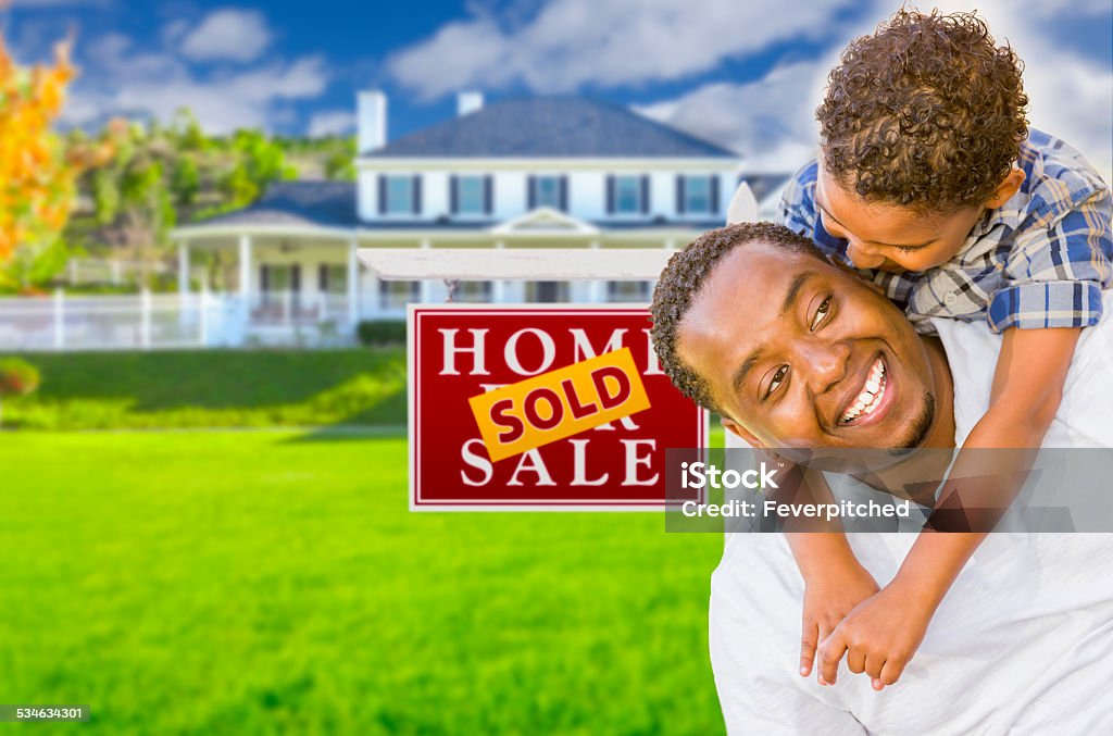 Father and Son In Front of Sold Sign and House Happy Mixed Race Father and Son In Front of Sold Real Estate Sign and New House. For Sale Sign Stock Photo