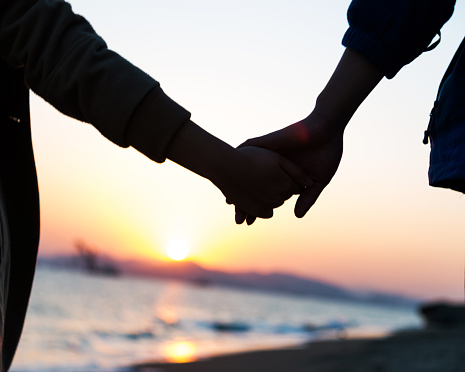 A couple holding hands in front of the sea at sunset.