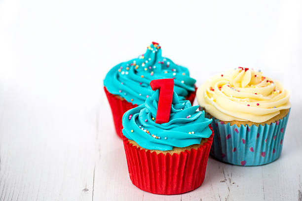 Composition of three tasty looking cupcakes in vivid blue, red and butter cream colours on white timber surface with shallow depth of field. The front baked pastry is with red sugar made number one in sharp focus. Aligned for perfect symmetry to allow equal copy space on both sides. Indoors studio shot with Canon EOS.