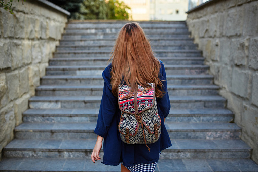 Student girl with a backpack climbing stairs. Rear view