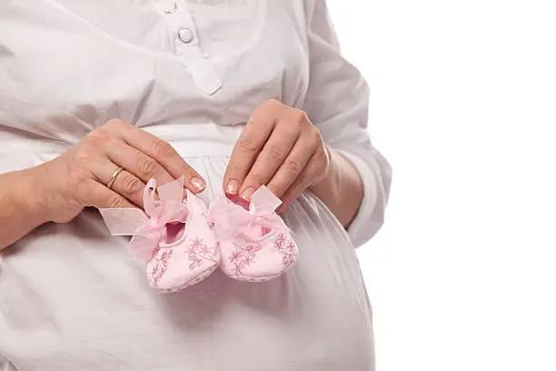 Pregnant woman keeping pink baby-shoes. Close up shot of belly and shoes.