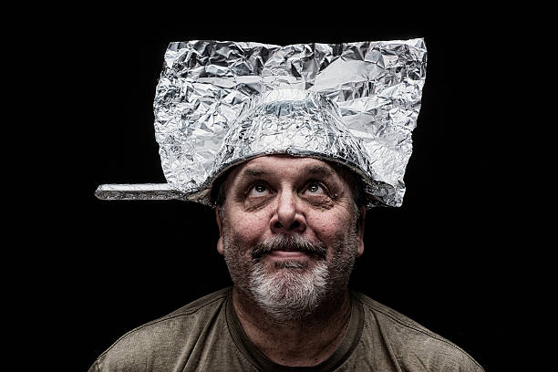 Crazy Guy wearing a colander as a hat A crazy guy trying to pick up radio signals with tin foil and wearinig an aluminum foil covered colander as a hat against a black background tin foil hat stock pictures, royalty-free photos & images