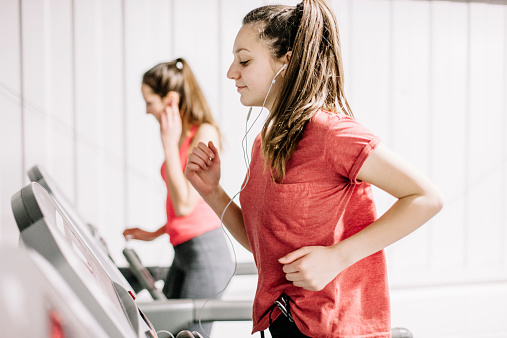 Two young women using running machines, wearing earphones and listening to music