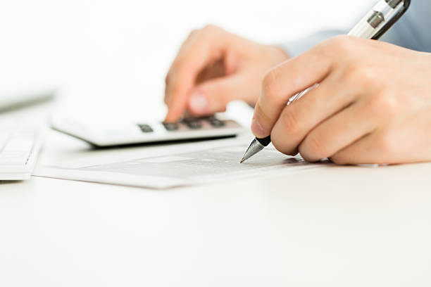 Hands of a male accountant writing and filling financial forms, calculating taxes, using calculator.