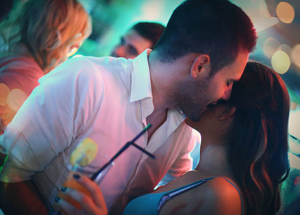 Group of young adults on double date in a club. Group of young adults in late 20's enjoying their night out in a club.Toasting with drinks,laughing and having casual conversation. Two couples on a double date.The guy is whispering to her ear. whisper men stock pictures, royalty-free photos & images