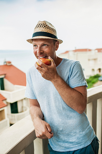 Man on a balcony eating a pear