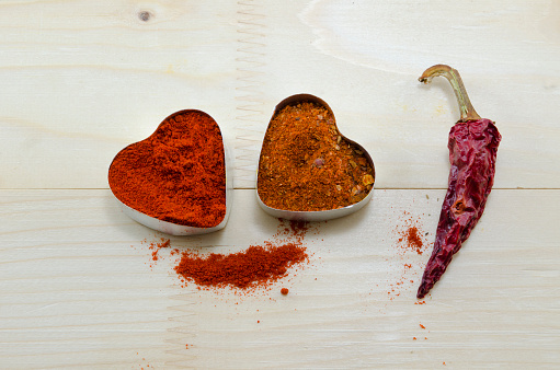 Two pepper hearts and a dried paprika on a wooden table