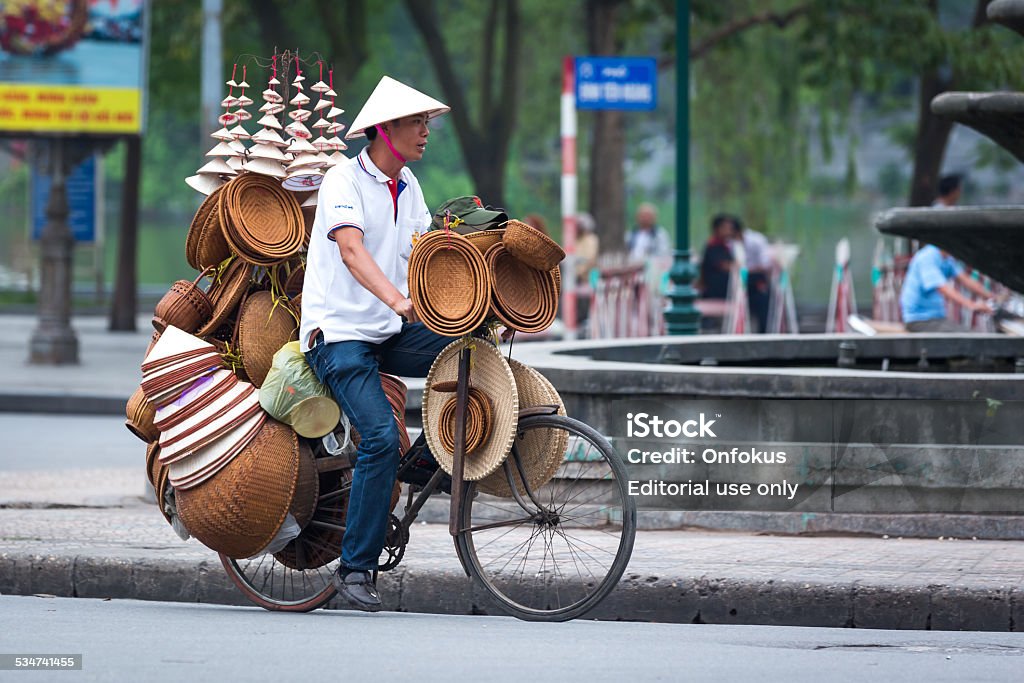 Street vendor in Hanoi, Vietnam Hanoi, Vietnam - March 29, 2013: A man is carrying his loaded bicycle with hats through the crowds of the city of Hanoi, Vietnam. 2015 Stock Photo