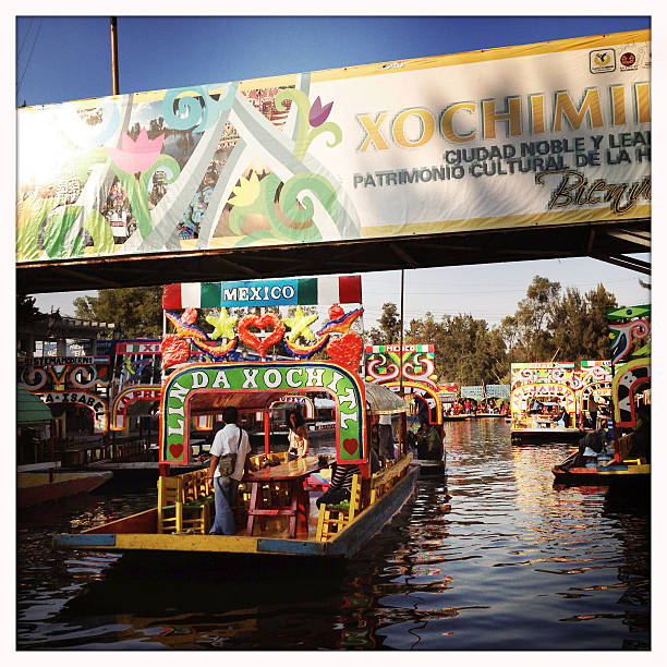 Trajinera boats in Xochimilco, Mexico City Xochimilco, Mexico - December 30, 2014: Traffic on the canals of Xochimilco, the "Mexican Venice". Close to Mexico City, it is a famous place to take a relaxing boat ride in the big Trajinera boats, which hold up to 20 people and have a meal and music on board. Small boats of vendors sell souvenirs, food and drink. trajinera stock pictures, royalty-free photos & images