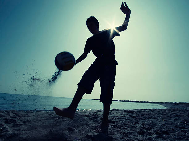 Two girls playing barefoot with a soccer ball on a sandy beach