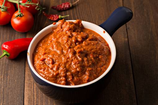 A high angle extreme close up, horizontal photograph of a blue bowl containing some homemade Harissa. Harissa is a Maghrebian (Northwest African) hot pepper paste made with roasted red bell peppers, a variety of fresh and dried chili peppers, garlic and tomato paste.