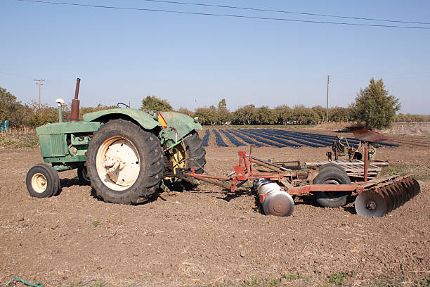 Farming tractor a farm tractor with a plow on the back with farm rows in the background. farmer tractor iowa farm stock pictures, royalty-free photos & images