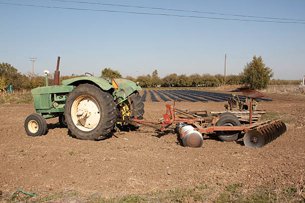 Farming tractor a farm tractor with a plow on the back with farm rows in the background. farmer tractor iowa farm stock pictures, royalty-free photos & images