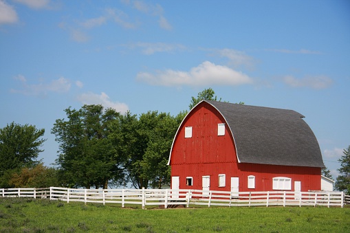A red, Gothic-style barn, white fence, and blue sky showcase the beauty of rural Iowa in the southwest region of the state. 
