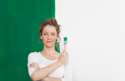 young woman standing in front of a self painted wall with a brush