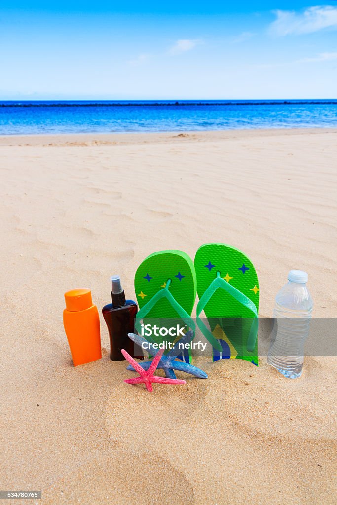 sandals and  bottle of water on sandy beach sandals and  bottle of water and suntan creams on sandy beach by sea side 2015 Stock Photo