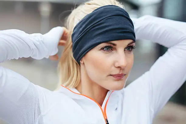 Close-up of young female athlete tying up hair  before a run. Sporty fitness woman on outdoor workout looking motivated.