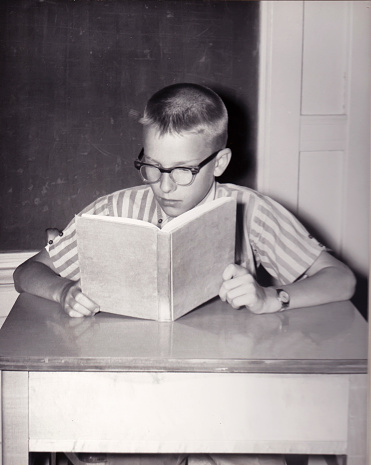 Vintage photograph of young boy reading a book at a desk in a school classroom