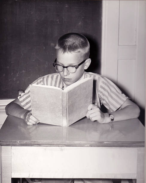 Vintage Photo of Young Boy Reading Book Vintage photograph of young boy reading a book at a desk in a school classroom textbook photos stock pictures, royalty-free photos & images