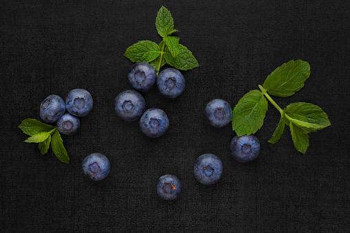 Blueberries isolated on black background with green mint leaves. Healthy fresh seasonal fruit eating.