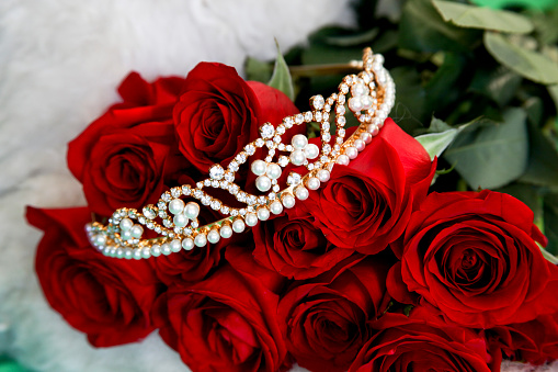 Pearl and rhinestone tiara laying across a dozen red roses