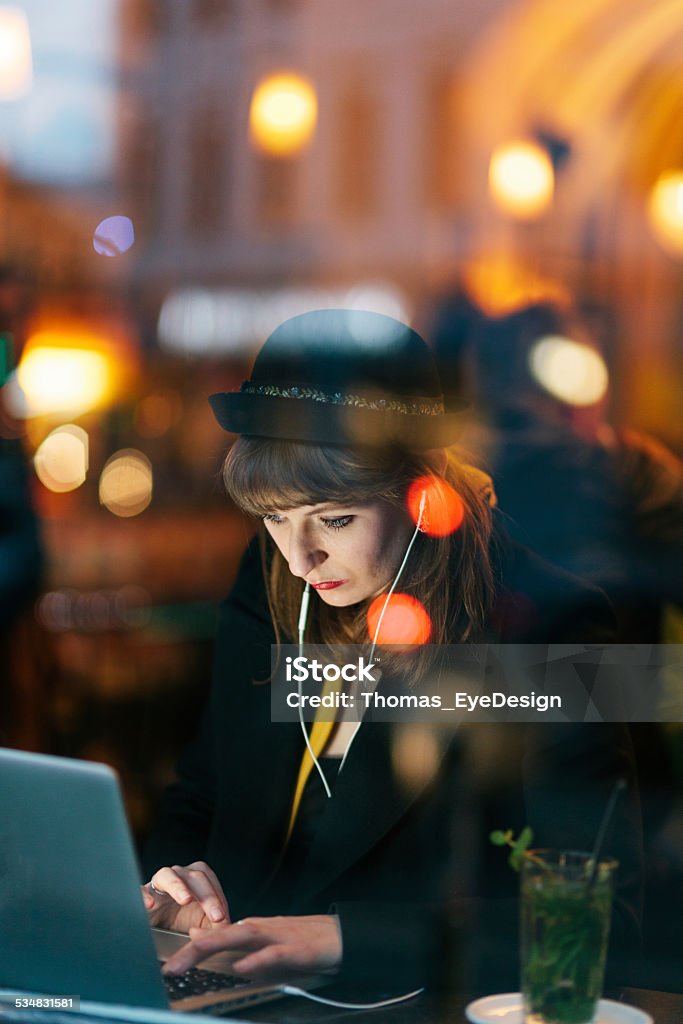 Woman in Cafe using Technology Woman sitting in Cafe at night using her Laptop and cellphone. City Stock Photo