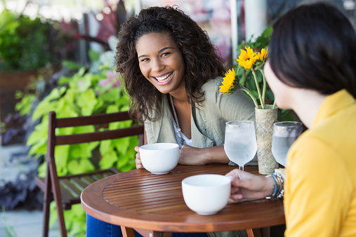 A mixed race, African American teenage girl with a friend, sitting at an outdoor table of a sidewalk cafe.