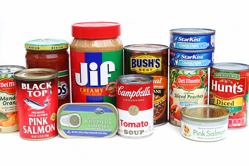 West Palm Beach, USA - October 8, 2014:  A studio shot of an assortment of canned foods. Foods include Campbell's tomato soup, Bush's baked beans, Del Monte peaches and mandarin oranges,  Star Kist tuna, Hunts diced tomatoes, Wild Planet sardines, Jif peanut butter, and Bear and Wolf salmon. These products are basic grocery staples found in many American kitlchens.
