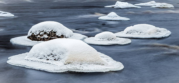 Snow covered rocks in stream stock photo