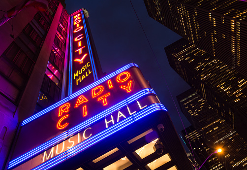 New York City, United States - August 12, 2014: The marquee of the world famous Radio City Music Hall along 6th Avenue in Midtown Manhattan is seen during the nighttime with office buildings in the background. The 6,015-seat theater is part of Rockefeller Center and opened on December 27, 1932 and is one of New York City's most popular tourist destinations. 