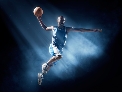 Close up image of professional basketball player about to do slam dunk during basketball game in floodlight