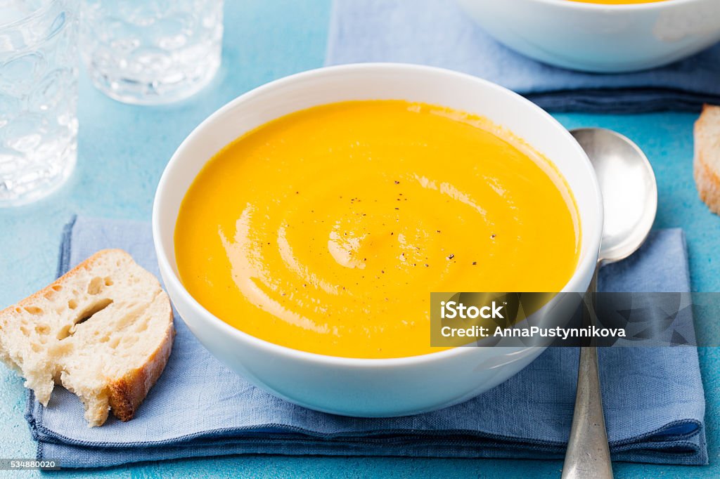 Pumpkin and carrot soup with cream on blue stone background. Pumpkin and carrot soup with cream on blue stone background American Culture Stock Photo