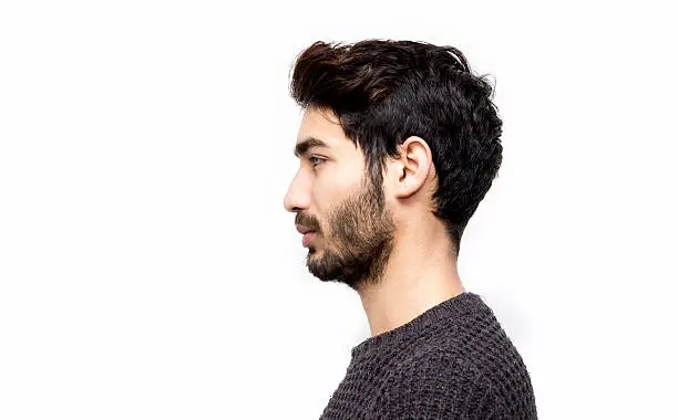 Profile view of serious young man over white background. Mug shot of young man isolated on white. Studio shot. Horizontal composition. Young man has got short black hair and beard.