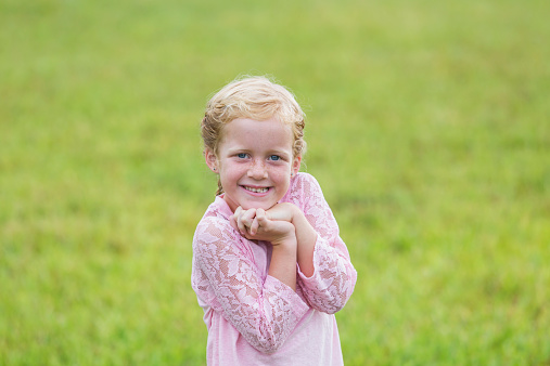 close-up of a smiley little girl in pink coat on green grass meadow