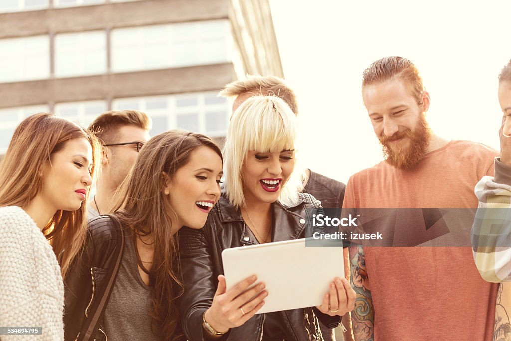 Group of friends using digital tablet outdoor Outdoor portrait of group of happy young people using a digital tablet together. Blond Hair Stock Photo