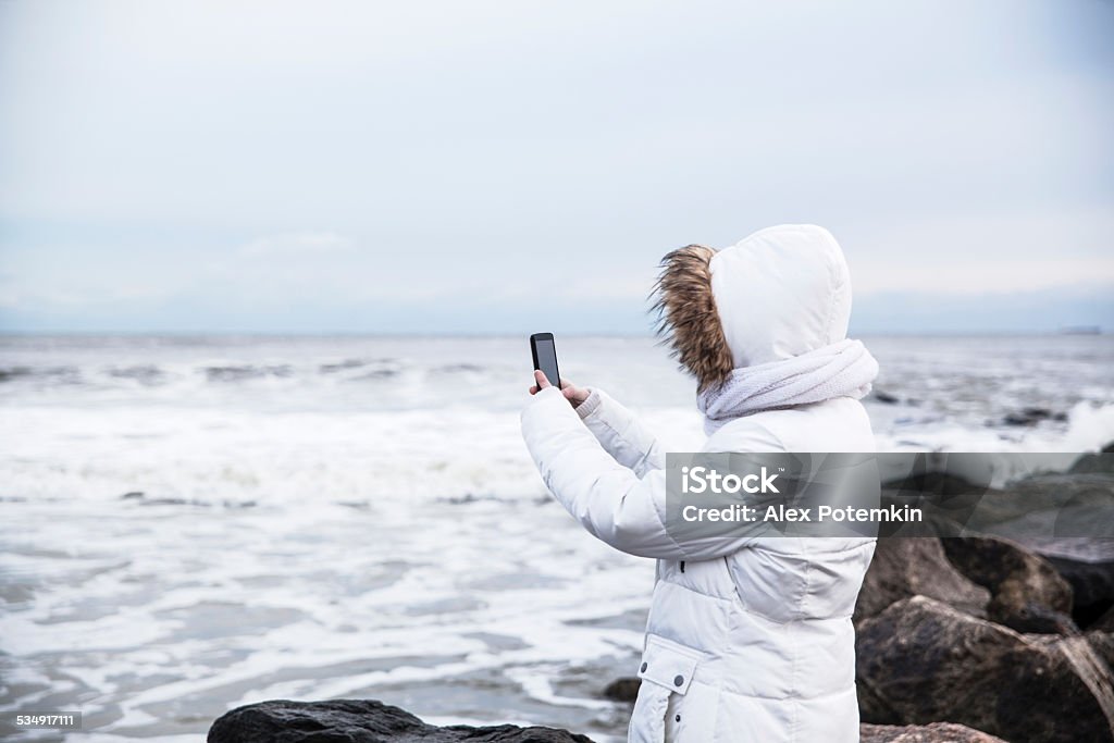Teenager girl make a picture with smartphone Teenager girl make a picture with smartphone  at the Long Beach, Long Island. Winter, cold windy weather, after the snowfall. 2015 Stock Photo