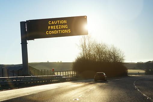 Motorway gantry sign in early morning winter sunshine reading caution freezing conditions