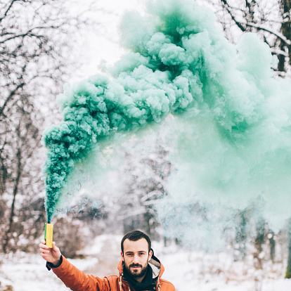Photo of a young man holding smoke coloured bomb in the nature