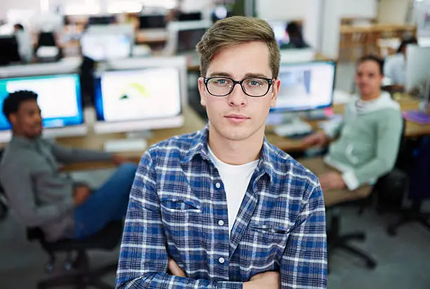 Portrait of a young man standing in an office with designers in the background