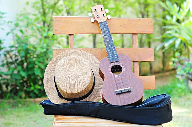 Photo of Brown Ukulele with lovely hat placed on a wooden chair