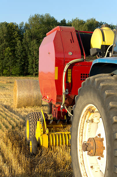 Close-up view of a farm tractor pulling in a wheat field Close up view of a farm tractor pulling a round baling machine in a wheat field after harvest.  hay baler stock pictures, royalty-free photos & images