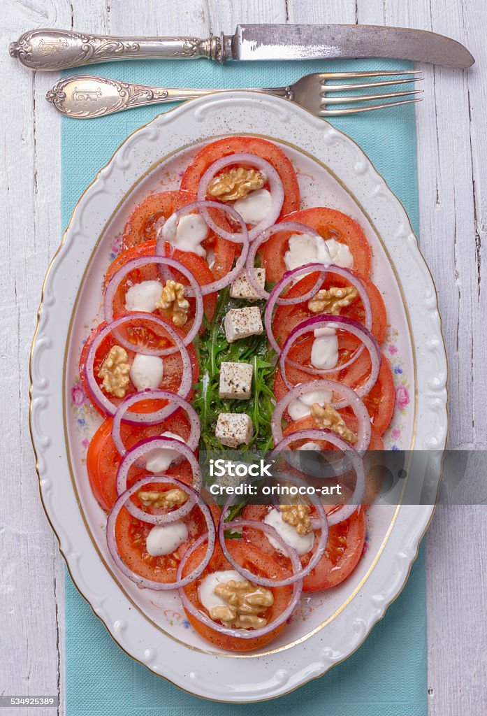 Tomato, Feta, Onions and Arugula Salad Tomato, Feta, Onions and Arugula Salad in a white bowl on white wooden background with antique fork and knife 2015 Stock Photo