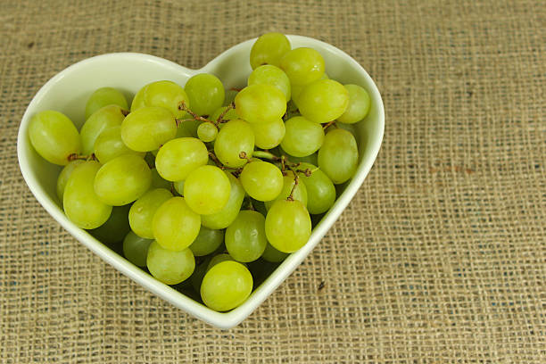 Green grapes in a heart shaped bowl on a rustic background stock photo