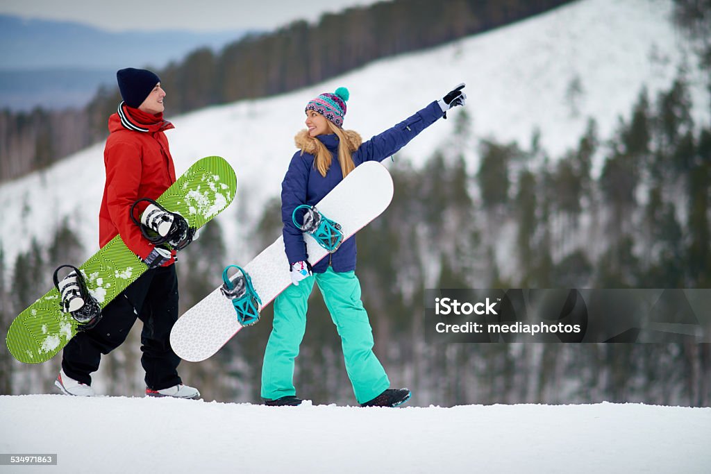 Mountains are calling Young couple walking with snowboards, woman pointing at slope 2015 Stock Photo