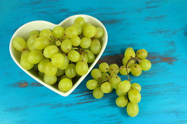 Green grapes in heart shaped bowl on a turquoise background stock photo